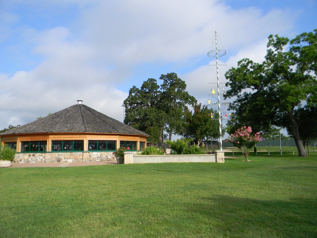 Fireman's park carousel building, a lawn, trees, and maypole